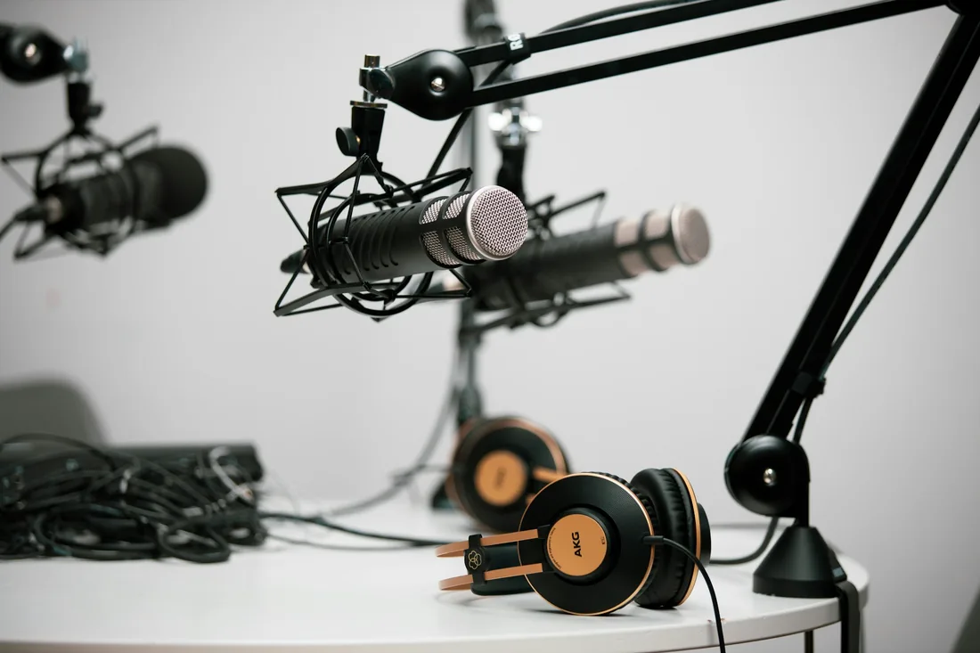 Varios micrófonos de estudio montados en brazos articulados sobre una mesa de grabación con auriculares
